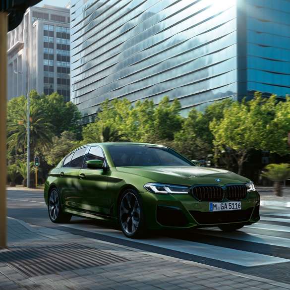 BMW M550i xDrive Sedan G30 LCI Facelift 2020 three-quarter front view driving BMW M550i xDrive Sedan G30 LCI Facelift 2020 BMW Individual Verde Ermes metallic three-quarter front view driving downtown
