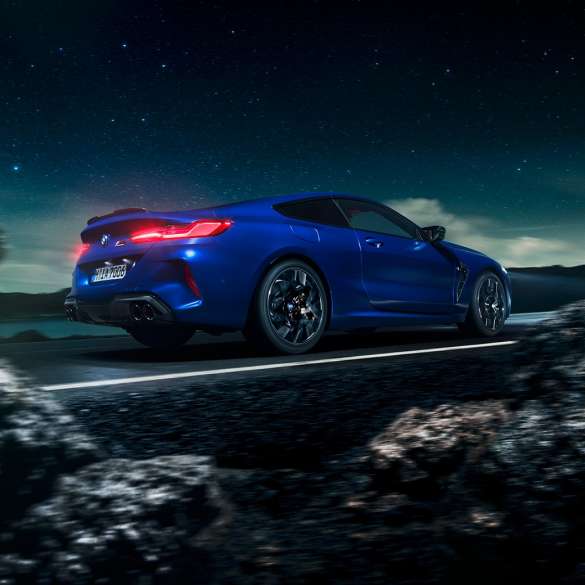 BMW M8 Competition Coupé, three-quarter side view. BMW M8 Competition Coupé in Marina Bay Blue metallic, driving three-quarter side view in front of starry sky.