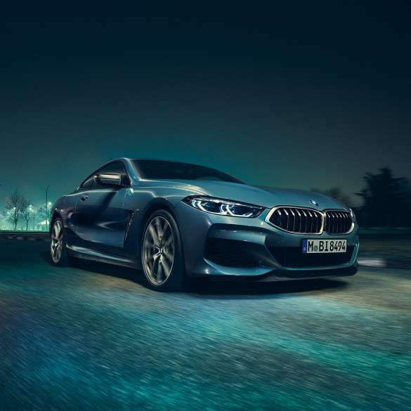 BMW M850i xDrive Coupé, three-quarter front view left. BMW M850i xDrive Coupé in Barcelona Blue metallic, three-quarter front view left, driving at night.
