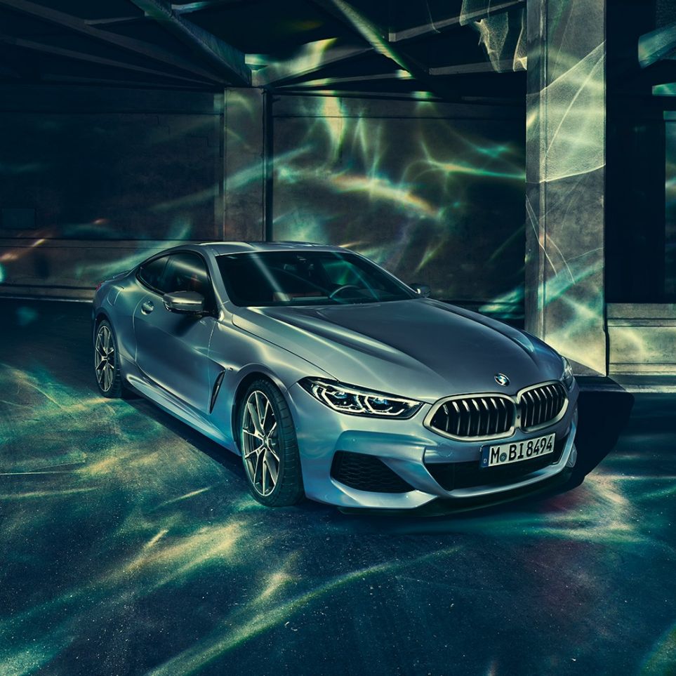 BMW M850i xDrive Coupé, three-quarter front view left. BMW M850i xDrive Coupé in Barcelona Blue metallic, three-quarter front view left, standing in front of building.