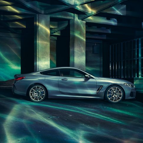 BMW M850i xDrive Coupé, side view. BMW M850i xDrive Coupé in Barcelona Blue metallic, side view, standing in front of building.