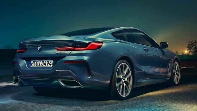 BMW M850i xDrive Coupé, rear view. BMW M850i xDrive Coupé in Barcelona Blue metallic, rear view, driving at night.