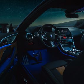 Interior BMW M8 Competition Coupé. BMW M8 Competition Coupé, interior at night with M leather steering wheel and blue ambient light with open driver door.