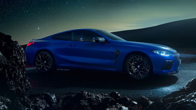 BMW M8 Competition Coupé, three-quarter side view. BMW M8 Competition Coupé in Marina Bay Blue metallic, standing three-quarter side view at night.