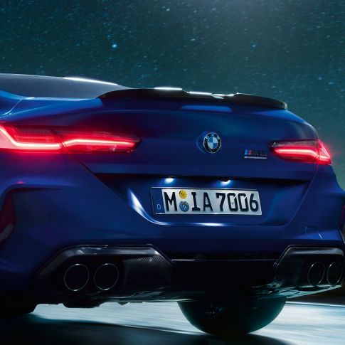 M diffuser in Carbon Black. BMW M8 Competition Coupé in Marina Bay Blue metallic, close-up rear at night with M diffuser in Carbon Black.
