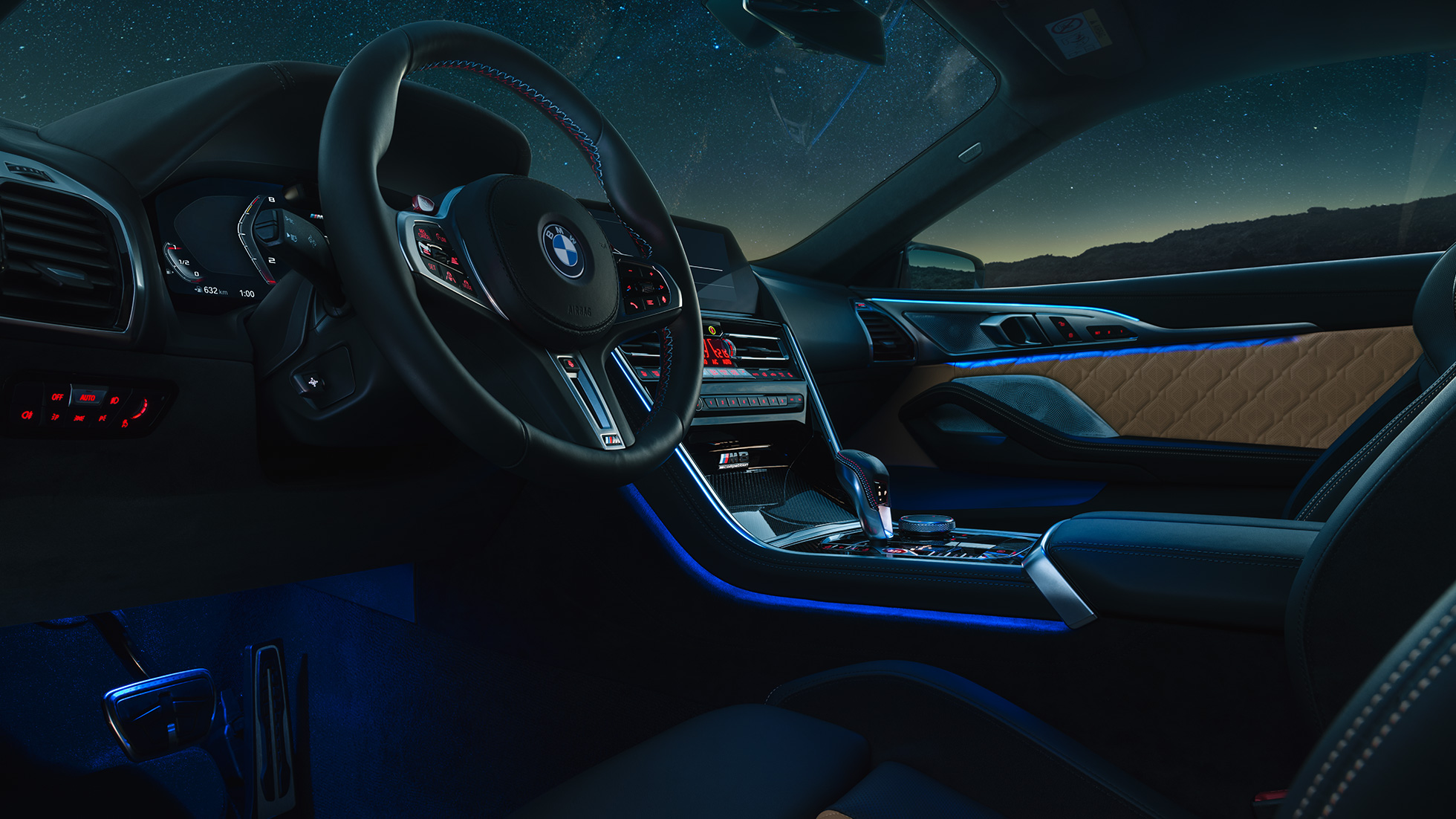 BMW M8 Competition Coupé, cockpit. BMW M8 Competition Coupé, cockpit at night with M leather steering wheel and blue ambient light.