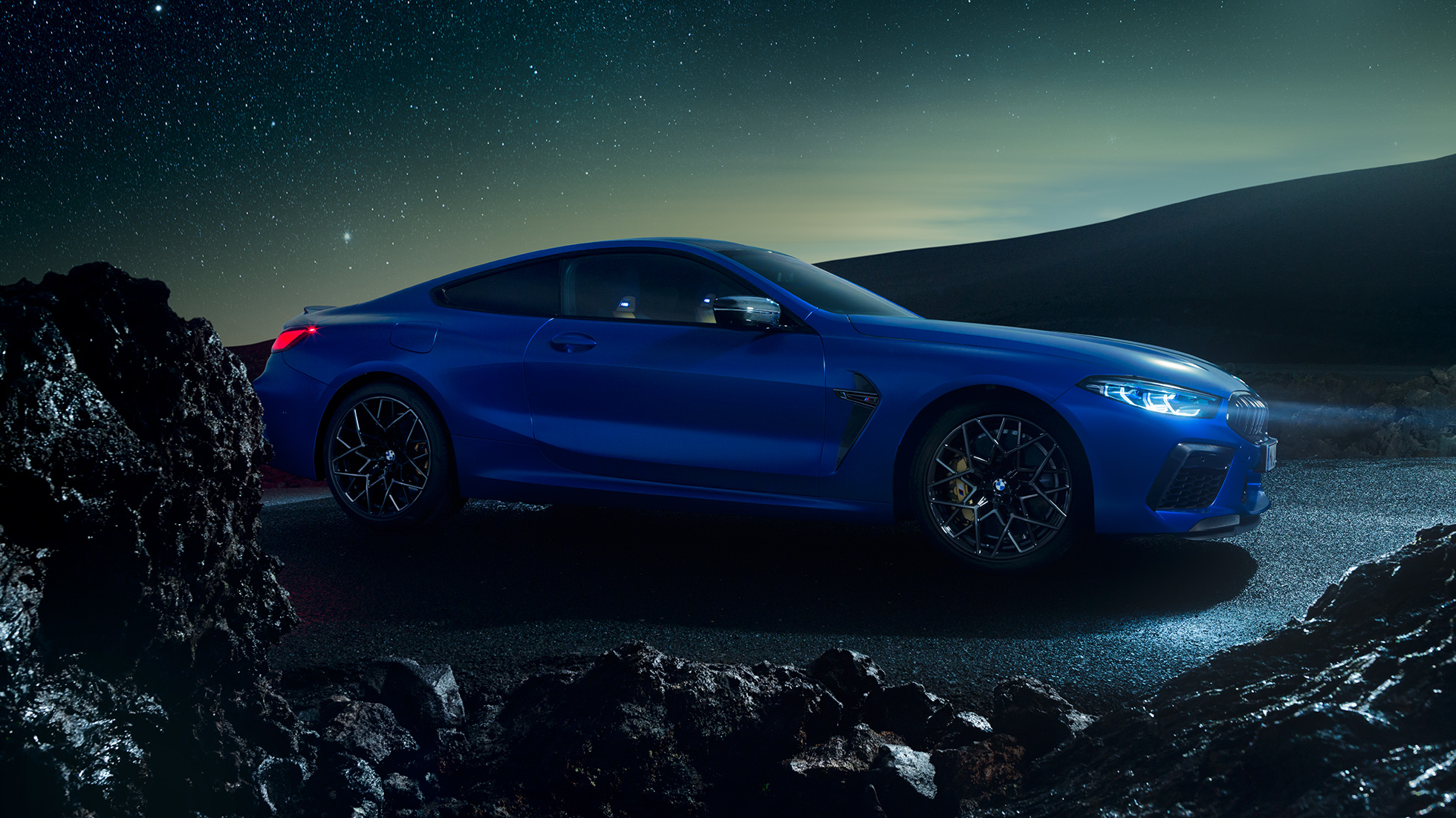 BMW M8 Competition Coupé, three-quarter side view. BMW M8 Competition Coupé in Marina Bay Blue metallic, standing three-quarter side view at night.