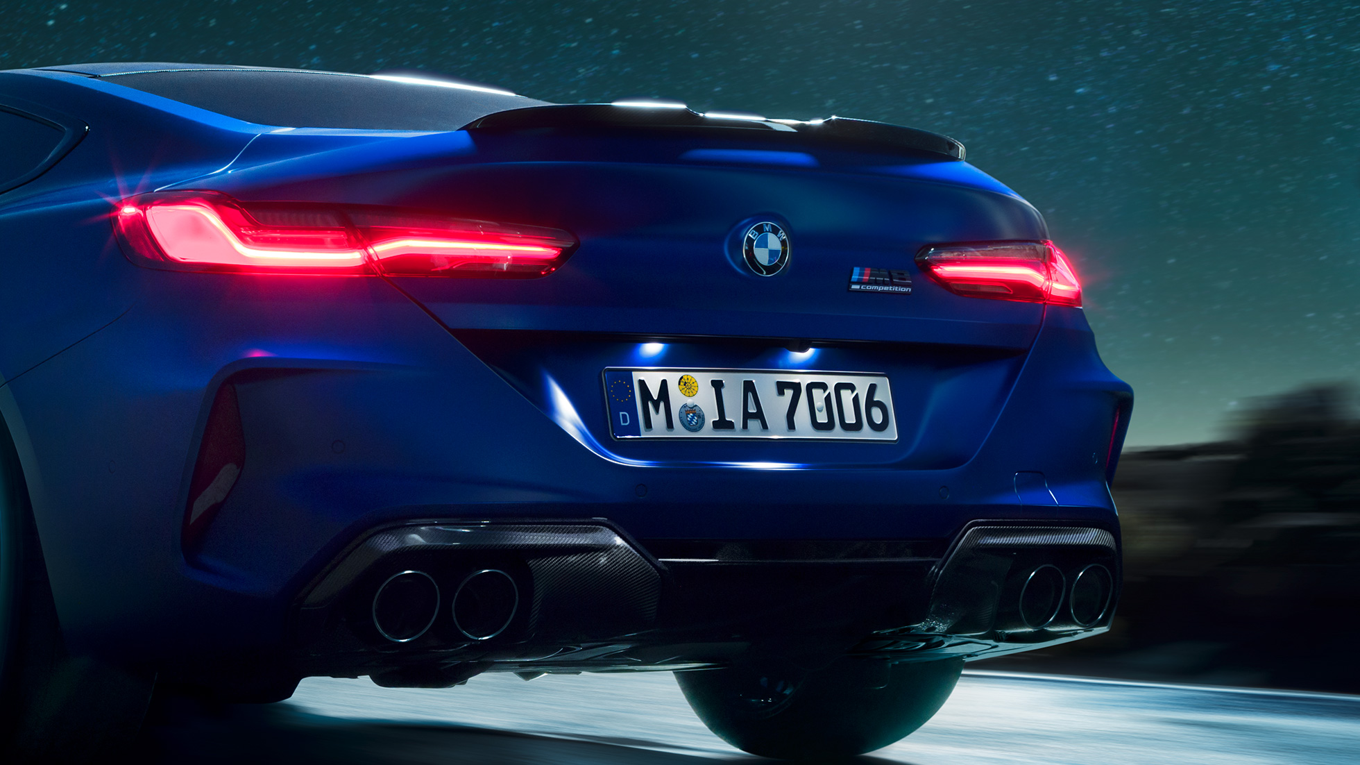 M diffuser in Carbon Black. BMW M8 Competition Coupé in Marina Bay Blue metallic, close-up rear at night with M diffuser in Carbon Black.