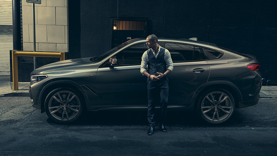 Man leaning on BMW X6 M50i in lateral perspective in front of an urban setting G06 2018 SUV