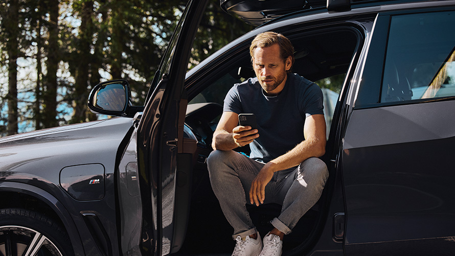 Man sitting in a BMW looking at his smartphone BMW Spring Summer Accessories Man sitting in a BMW looking at his smartphone
