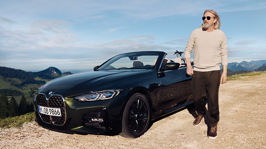 Man walking next to a BMW in front of mountain landscape  BMW Spring Summer Accessories Man walking next to a BMW in front of mountain landscape